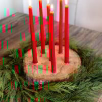 Tree trunk slice taper candle holder for Christmas with cedar branches around it.
