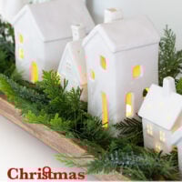 Christmas tabletop display using white ceramic houses lined up in a dough bowl with greenery around them.